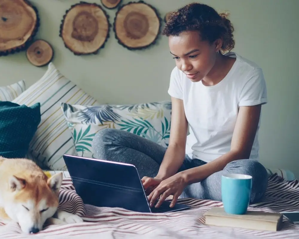 A woman on her laptop with her dog asleep beside her