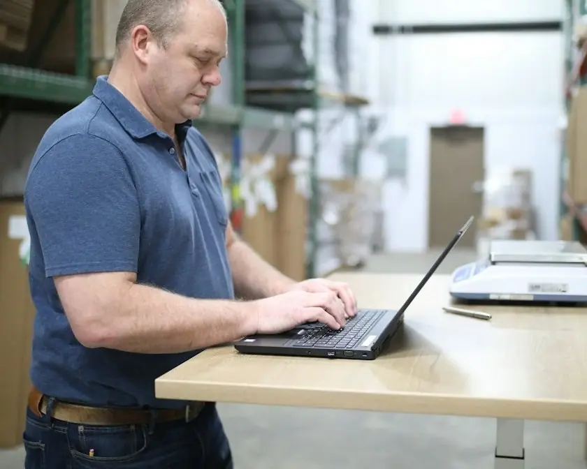 A man working at a standing desk in a warehouse