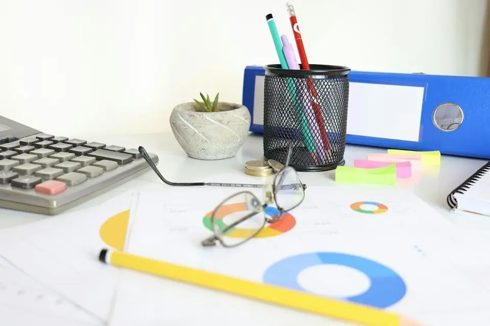 A desk with a calculator, glasses and printed charts