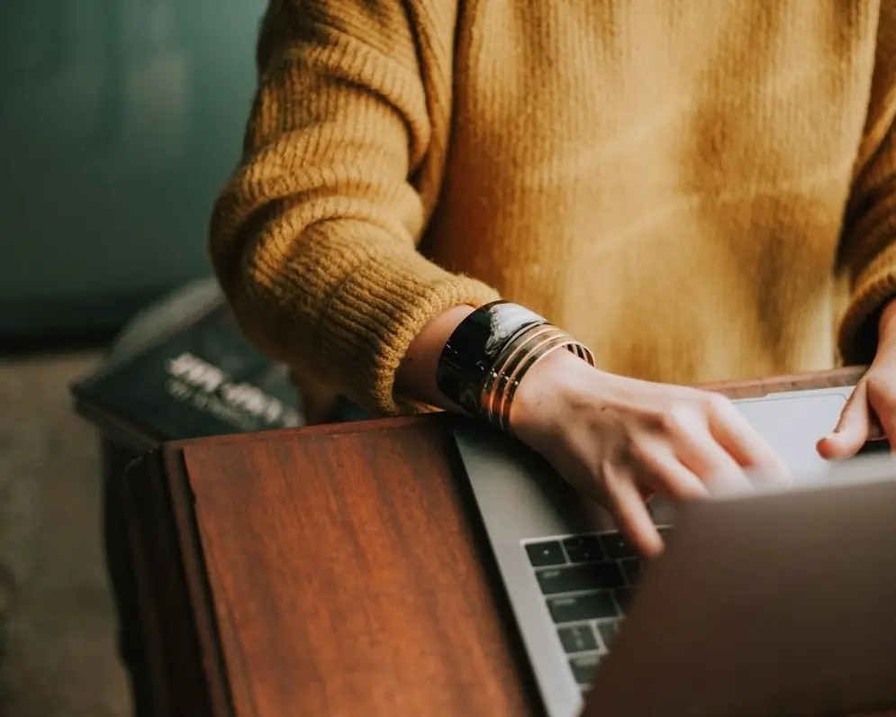 A person in a mustard sweater typing on a laptop