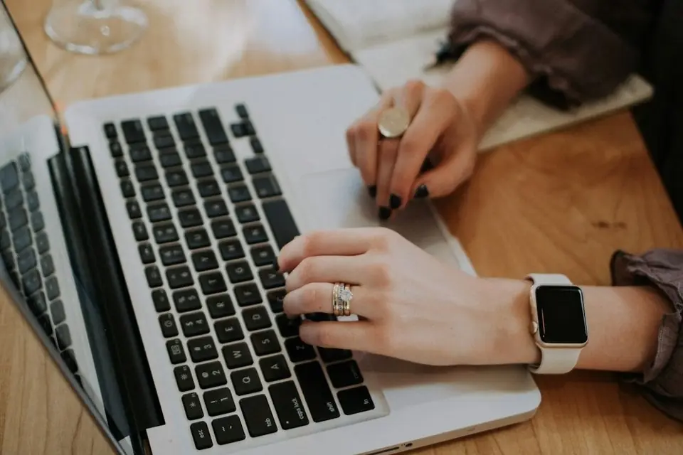 Hands typing on a laptop at a wooden table