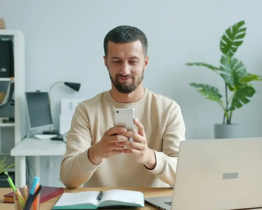 A man smiling at his phone at his desk