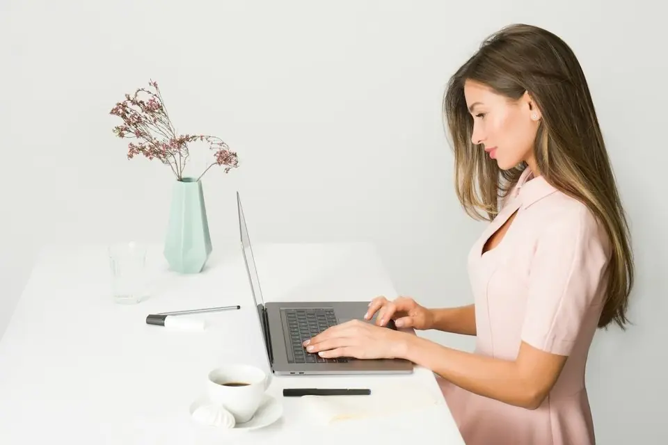 A woman typing on a laptop at a white desk