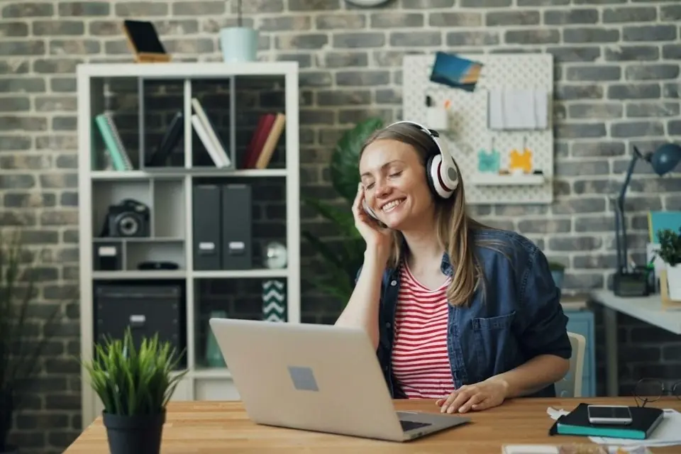 A woman in headphones at her laptop in a brick walled office